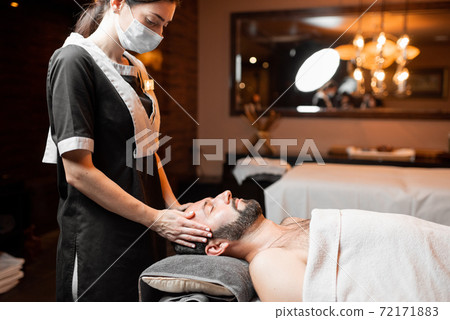 Female masseur doing facial massage to a male client Female masseur doing facial massage to a male client 72171883