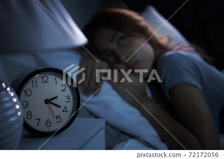Depressed young woman lying in bed cannot sleep from insomnia. Selective focus on alarm clock 72172056