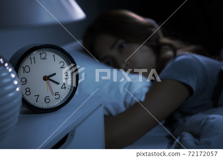 Depressed young woman lying in bed cannot sleep from insomnia. Selective focus on alarm clock 72172057