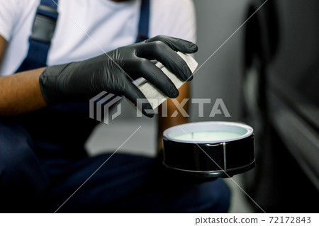 Car detailing, tools for polishing. Professional auto care products. Cropped close up shot of worker hands in gloves, holding the jar with solid carnauba wax to polish the car body Car detailing, tools for polishing. Professional auto care products. Cropped close up shot of worker hands in gloves, holding the jar with solid carnauba wax to polish the car body 72172843