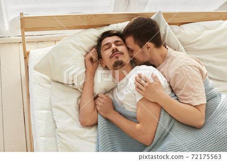 Happy gay couple lying on bed at home Happy gay couple lying on bed at home 72175563