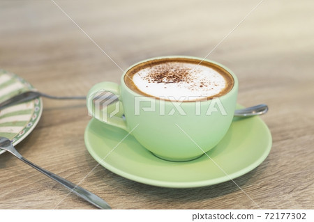 Green Cup Of Coffee Latte On Wooden Background, Close Up Of Art Coffee In Morning. Green Cup Of Coffee Latte On Wooden Background, Close Up Of Art Coffee In Morning. 72177302