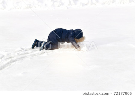 A child crawls on all fours in the snow in a winter jumpsuit with a fur hood. A child crawls on all fours in the snow in a winter jumpsuit with a fur hood. 72177906