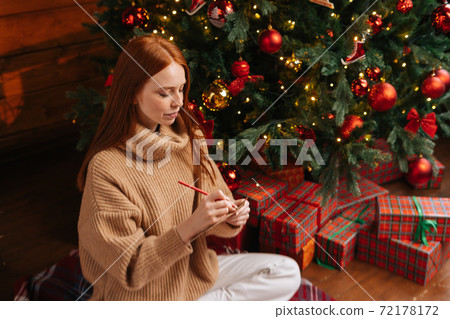 High-angle shot of dreamy young woman writing wish list for new year on background of Christmas tree High-angle shot of dreamy young woman writing wish list for new year on background of Christmas tree 72178172