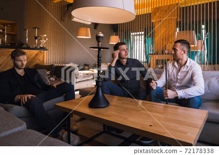 Men relax and smoke hookah in a stylish loft cafe with a modern design 72178338