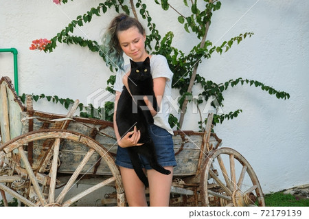 Teenager girl holding big black cat in her arms, outdoor 72179139