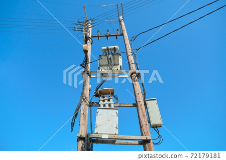 Electric transformer on wooden poles, blue sky background 72179181