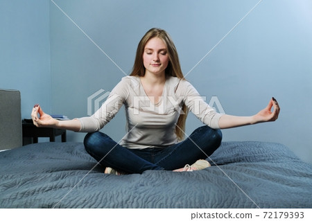 Relaxed young woman sitting at home in bed meditating girl practicing yoga Relaxed young woman sitting at home in bed meditating girl practicing yoga 72179393