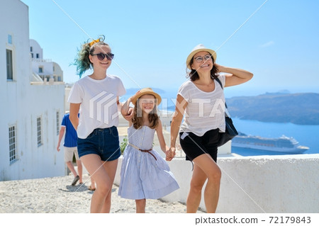 Mother walking with two daughters holding hand in Santorini island 72179843