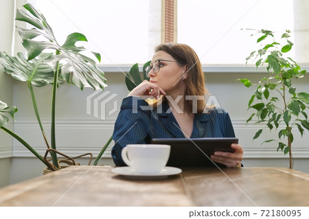 Serious mature woman having breakfast at home reading digital tablet 72180095