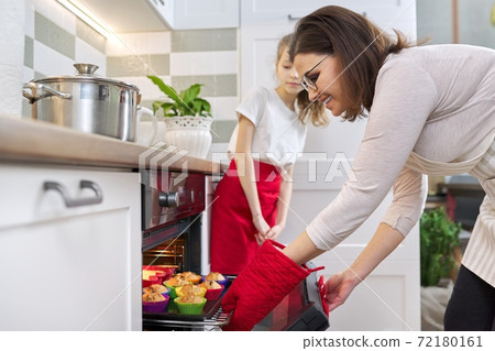 Mother taking out tray with baked cupcakes from oven Mother taking out tray with baked cupcakes from oven 72180161