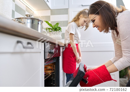 Mother taking out tray with baked cupcakes from oven Mother taking out tray with baked cupcakes from oven 72180162