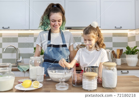 Two girls, teenager and younger sister, preparing cookies together in kitchen Two girls, teenager and younger sister, preparing cookies together in kitchen 72180218