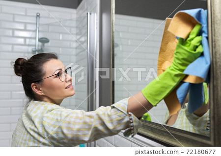 Woman cleaning mirror in bathroom using professional rag spray 72180677