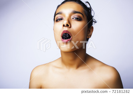 young pretty indian woman with dry fruit in mouth on white background young pretty indian woman with dry fruit in mouth on white background 72181282
