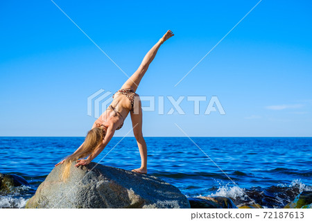 Slim female doing yoga against bright blue sky Slim female doing yoga against bright blue sky 72187613