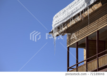 Roof with snow cornice and icicle at wooden house with balcony 72189048