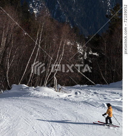 Skier descent on snowy ski slope in forest at sunny winter day Skier descent on snowy ski slope in forest at sunny winter day 72189052