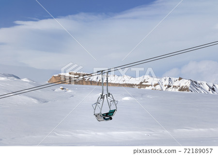 Snowy slope with new-fallen snow, ski-lift and blue sky with clouds Snowy slope with new-fallen snow, ski-lift and blue sky with clouds 72189057