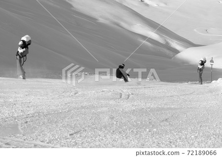 Snowboarder downhill on snowy ski slope with snow cannons at sun winter day 72189066