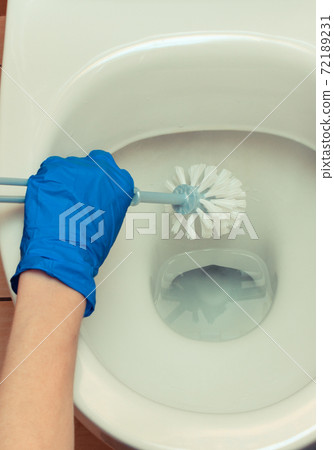Hand in blue glove cleaning toilet bowl using brush and chemical detegent 72189231