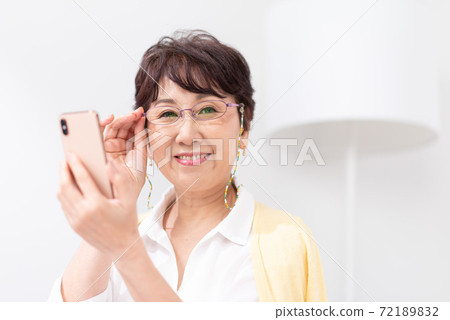 A woman looking at a smartphone with reading glasses 72189832