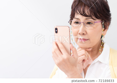 A woman looking at a smartphone with reading glasses 72189833