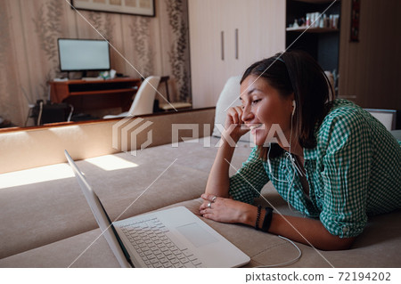 Young woman on sofa happily working on new project with laptop in home 72194202