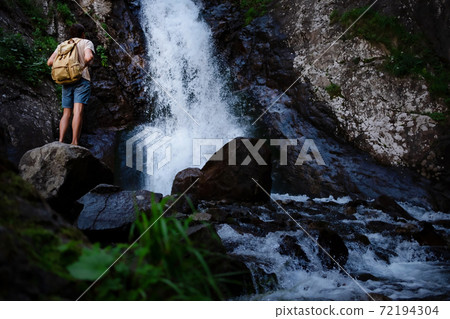 Hiker waalkinh with backpack looking at waterfall in park in beautiful nature landscape. 72194304