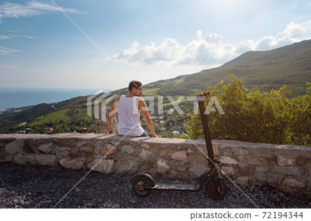 Young man riding an electric scooter on mountain range. Ecological transportation concept 72194344