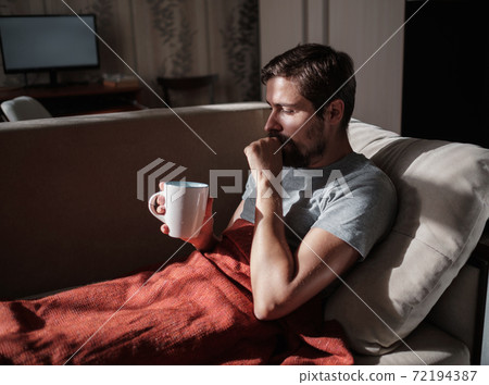 Young ill man drinking hot tea at home Young ill man drinking hot tea at home 72194387