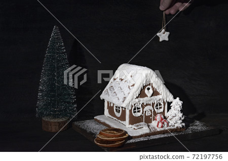 Gingerbread house next to small Christmas tree on dark background. Christmas composition 72197756