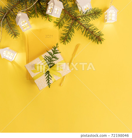 Xmas business greeting card. Yellow notepad on 2021, fir branches, shining Xmas lights white lodges, gift box on yellow. Planning for next year. Top view. Copy space for text. Square image. Xmas business greeting card. Yellow notepad on 2021, fir branches, shining Xmas lights white lodges, gift box on yellow. Planning for next year. Top view. Copy space for text. Square image. 72198046