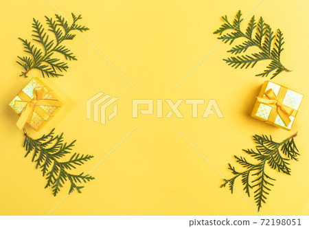 Christmas Or New Year greeting card with frame of two gift boxes and green arborvitae branches laid out on bright yellow with copy space in center. Xmas decorations. Top view. Horizontal orientation. Christmas Or New Year greeting card with frame of two gift boxes and green arborvitae branches laid out on bright yellow with copy space in center. Xmas decorations. Top view. Horizontal orientation. 72198051