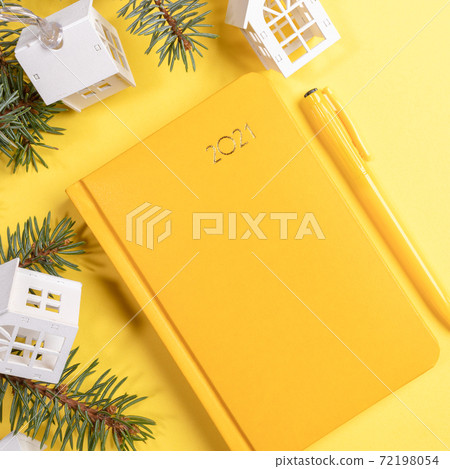 Xmas festive workspace close up. Yellow background with notepad-organizer on 2021, fir branches and Xmas lights white lodges. Planning for next year. Business greeting card. Top view. Copy space. Xmas festive workspace close up. Yellow background with notepad-organizer on 2021, fir branches and Xmas lights white lodges. Planning for next year. Business greeting card. Top view. Copy space. 72198054