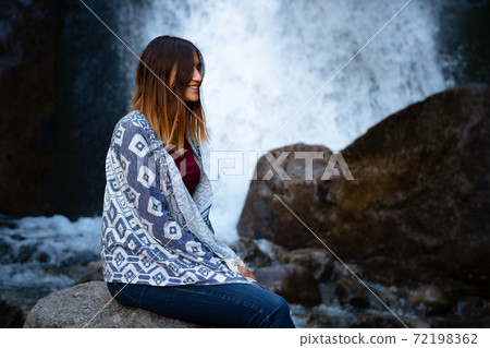 Beautiful young woman hiker sitting near waterfall Beautiful young woman hiker sitting near waterfall 72198362