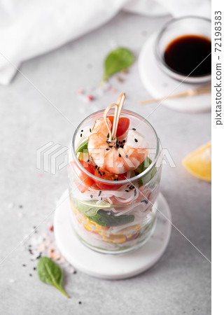 rice noodles with shrimps and vegetables in a glass jar on a white table 72198383