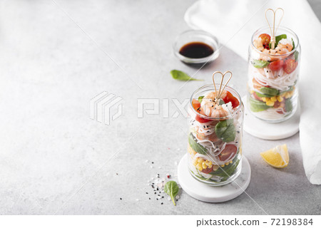 rice noodles with shrimps and vegetables in a glass jar on a white table 72198384