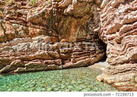 The sea view. Entrance to the cave from the sea. Calm clear sea. The rock consists of layered stones. Montenegro The sea view. Entrance to the cave from the sea. Calm clear sea. The rock consists of layered stones. Montenegro 72198713