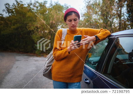 Woman beside a car and looking at smart phone. 72198795
