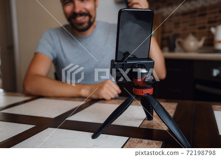Young man having video call via smartphone in the home office. Young man having video call via smartphone in the home office. 72198798