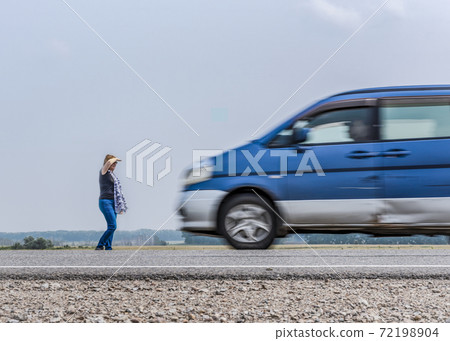 Blurred silhouettes of a fast-moving car and a woman standing on the side of the road Blurred silhouettes of a fast-moving car and a woman standing on the side of the road 72198904