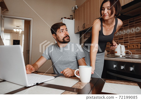 Couple at kitchen, reading news and using laptop. Couple at kitchen, reading news and using laptop. 72199085