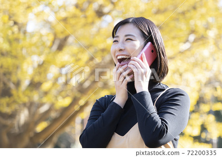 一個女人在秋天公園帶著微笑打電話 一個女人在秋天公園帶著微笑打電話 72200335