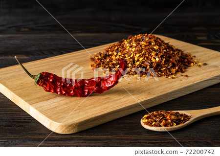 Red hot chilli pepper dry pod and flakes on a cutting board over black wood table. 72200742