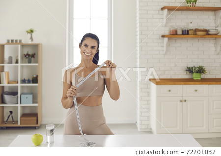 Portrait of a female sports coach and dietitian standing with a tape measure in her hands. 72201032