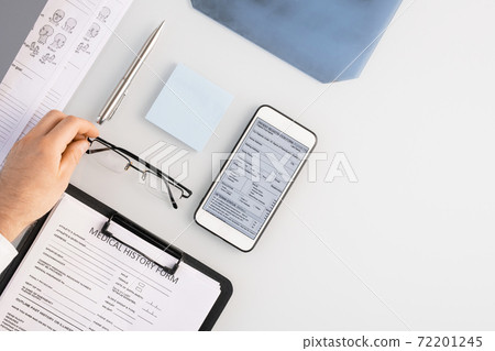Flatlay of hand of doctor putting eyeglasses on table by medical history form 72201245
