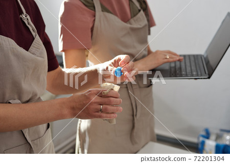 Hand of female in apron putting handmade blue glass bead into small linen sack Hand of female in apron putting handmade blue glass bead into small linen sack 72201304