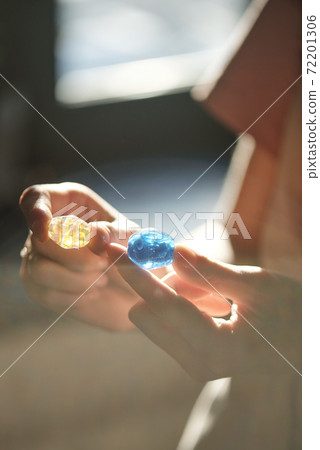 Hands of young female artisan holding blue and yellows handmade glass beads 72201306