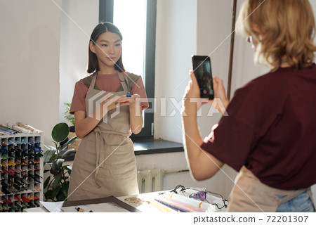 Young brunette woman with handmade glass bead on hand standing by workplace Young brunette woman with handmade glass bead on hand standing by workplace 72201307